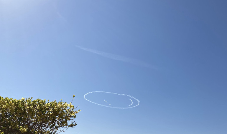 Smiley face written in white against a blue sky by a small unseen plane. Photo by Judy Darley