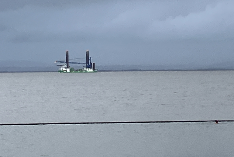 Oil rig at Clevedon Marine Lake. Photo by Judy Darley. Taken on New Year's Day 2024. Stormy skies above and swimmer just visible in foreground.